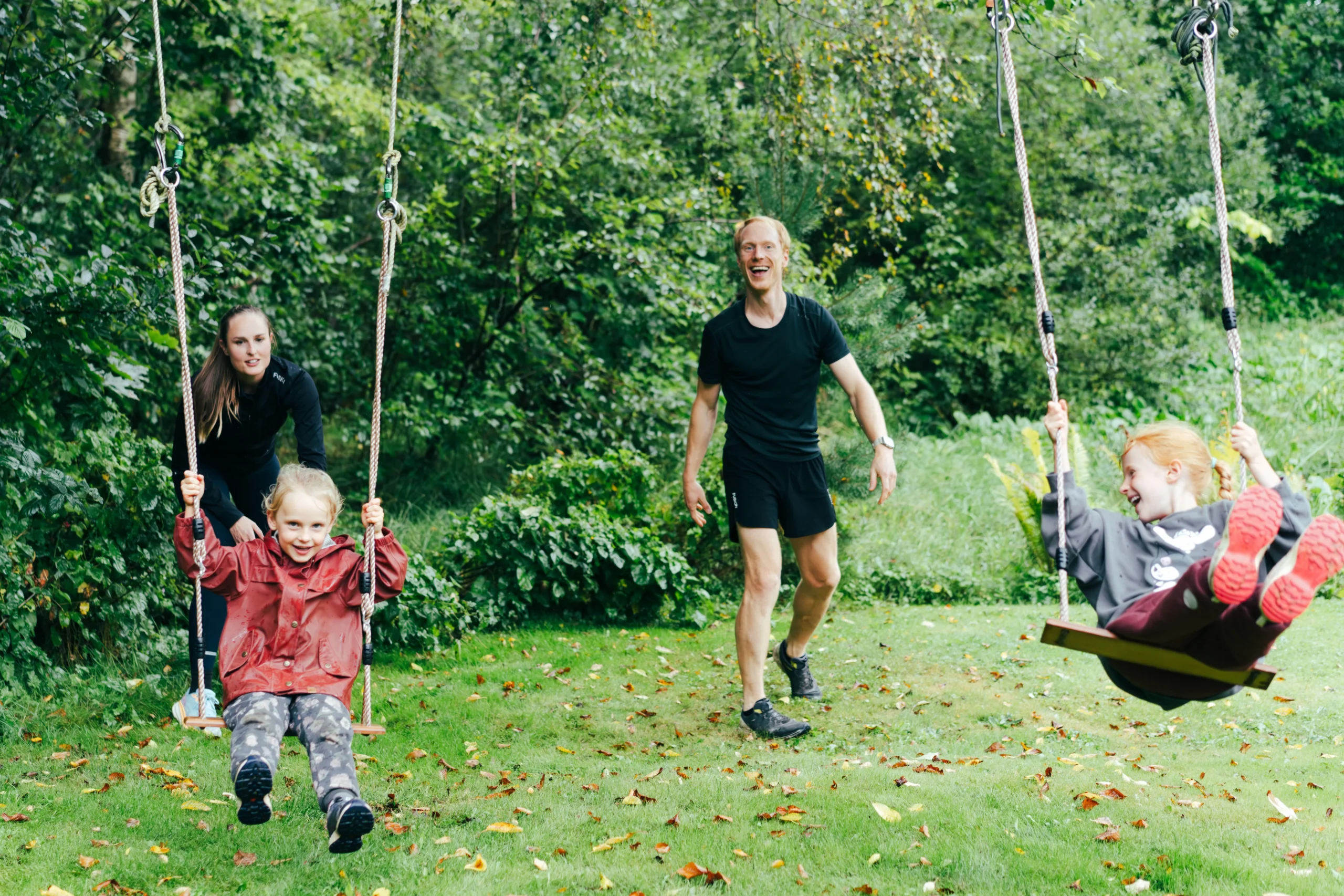 Mor og far gynger deres to piger i haven
