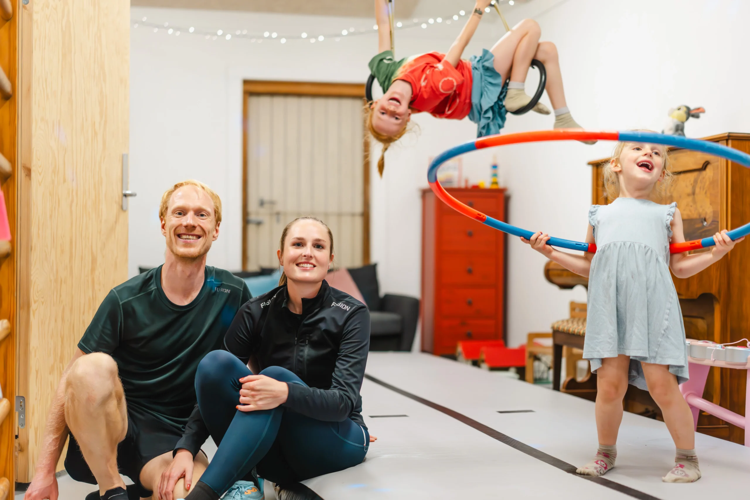 de to piger svinger sig i gynger og hulahopring imens forældrene sidder og ser på